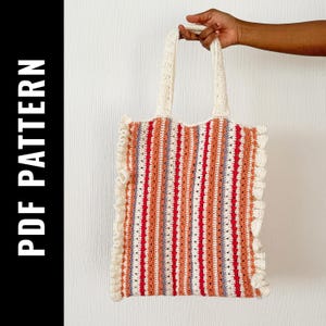 Puede incluir: Un bolso de mano de crochet con un diseño a rayas en tonos rojos, naranjas, blancos y morados. El bolso tiene un borde con volantes y correas blancas.
