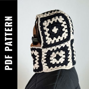 Puede incluir: Cuello de capucha de crochet negro y beige con un patrón cuadrado. El cuello está siendo usado por una persona con trenzas.