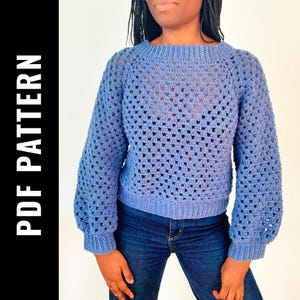 Puede incluir: Un suéter de crochet azul con un patrón de punto cuadrado. El suéter tiene un cuello redondo y mangas largas.