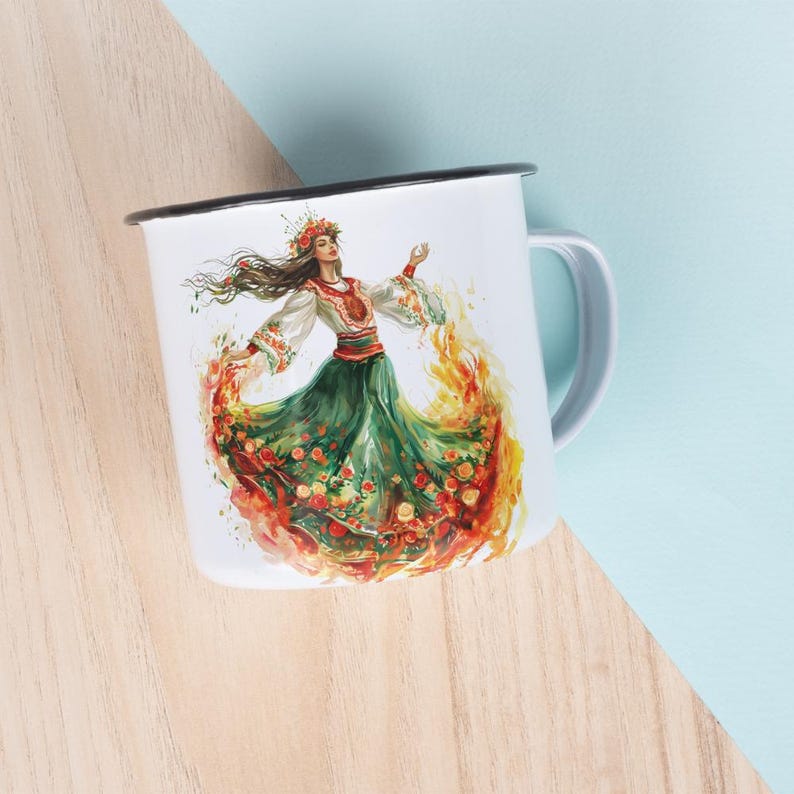Puede incluir: Taza de esmalte blanco con una ilustraci&oacute;n colorida de una mujer con un vestido verde y rojo bailando con llamas a su alrededor. La mujer lleva una corona de flores y una blusa blanca bordada.