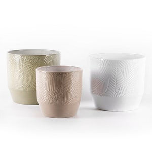 Può includere: Tre vasi in ceramica di diverse dimensioni con un motivo a foglie geometriche. I vasi sono in tonalità di verde, marrone e bianco.