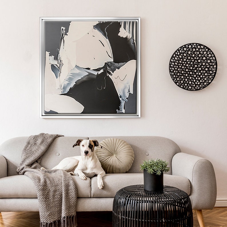 May include: A white dog with black and brown spots is lying on a light gray couch with a brown throw blanket. There is a black and white abstract painting on the wall behind the couch. A black wicker side table is in front of the couch.
