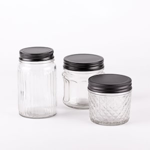 Può includere: Tre barattoli di vetro con coperchi in metallo nero. I barattoli hanno diverse texture: uno è liscio, uno è rigato e uno ha un motivo a rombi.