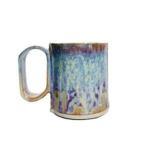 May include: A ceramic mug with a blue, purple, and yellow glaze. The mug has a rounded handle and a wide base.