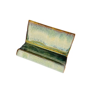 May include: A ceramic dish with a green and brown glaze. The dish is shaped like a small bench and has a slightly curved top.
