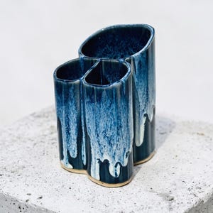 May include: A ceramic utensil holder featuring three connected cylindrical compartments with a glossy, reactive glaze in shades of deep navy blue and white, characterized by a distinctive drip pattern that cascades down the exterior surfaces.