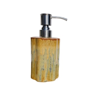 May include: A ceramic soap dispenser with a stainless steel pump. The dispenser is a mottled yellow and brown color with a textured surface.