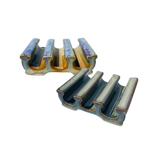 May include: Two ceramic wine bottle holders. One is a light blue, yellow, and purple color. The other is a dark teal color. Each holder has four slots for bottles and a curved design.