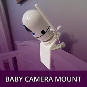 May include: A white baby monitor camera mounted on a purple crib rail with a white clamp. The camera has a black lens and a small antenna. The text "BABY CAMERA MOUNT" is displayed at the bottom of the image.
