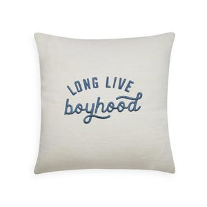 Op de afbeelding: Vierkantig crèmekleurig kussen met de geborduurde tekst "LONG LIVE boyhood" in blauw. Het kussen heeft een zacht, getextureerd uiterlijk en de letters zijn in cursieve stijl.