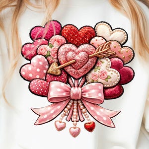 Könnte beinhalten: Weißes Sweatshirt mit einem Bouquet aus Herzen in verschiedenen Rosa- und Rottönen. Das Design umfasst eine große rosa Schleife mit einer Perlenkette und herzförmigen Anhängern. Ein goldener Pfeil durchbohrt ein zentrales Herz.
