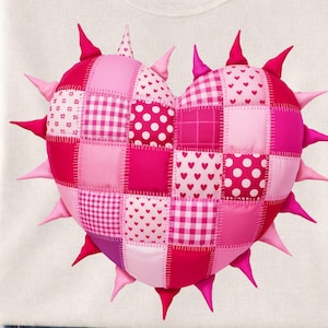 May include: A white t-shirt featuring a large, heart-shaped design. The heart is composed of various pink patchwork squares with different patterns, including polka dots, hearts, and gingham. Spikes of varying shades of pink surround the heart.