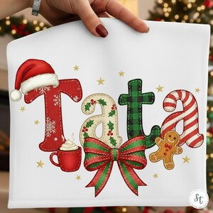 Peut inclure: Coussin décoratif blanc sur le thème de Noël avec le mot "Tata" en lettrage festif. Les lettres sont ornées d'éléments de vacances comme un bonnet de Père Noël, du houx, du tartan et des rayures de canne en sucre. Un bonhomme en pain d'épices et un nœud rouge complètent le design.