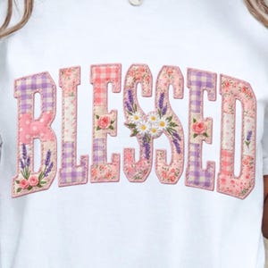 Könnte beinhalten: Weißes T-Shirt mit dem Wort "BLESSED" in einem Patchwork-Design. Die Buchstaben sind in Rosa, Lila und Weiß gehalten, mit Blumen- und Vichy-Mustern. Der Buchstabe "S" ist mit Gänseblümchen und Lavendel verziert.