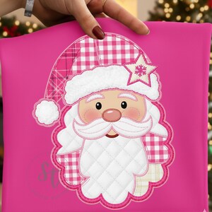 May include: A pink Santa Claus design with a white beard and hat trim, a star, and a pink and white checkered pattern. The Santa Claus design is on a pink background. The design is a festive holiday decoration.