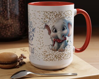 May include: White ceramic mug with a red interior and handle. The mug features a cartoon elephant design with a red scarf. The design includes gold speckles and text. The mug is on a wooden surface.