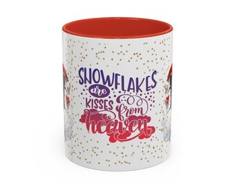 May include: White ceramic mug with a red interior and a festive design. The mug features the text "Snowflakes are kisses from heaven" in purple and red, with gold confetti accents. A cheerful winter-themed gift.