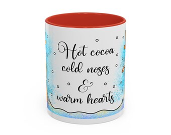 May include: White ceramic mug with a red interior. The mug has the text "Hot cocoa, cold noses & warm hearts" in black script. The design includes blue accents and small white dots, suggesting a winter theme.