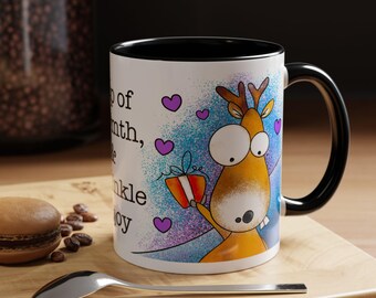 May include: White ceramic mug with a black interior and handle. The mug features a cartoon reindeer holding a gift, with purple hearts and text. The mug is on a wooden surface with a spoon and a pastry.