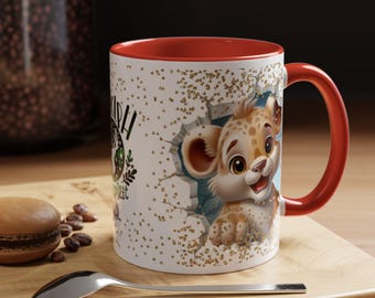 May include: White ceramic mug with a red interior and handle. The mug features a cartoon leopard breaking through a wall, with gold glitter accents. Text is visible on the side of the mug. A spoon and a pastry are in the foreground.