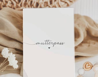 May include: A white card with the text "mutterpass" in black cursive script and a small black heart below the text. The card is on a white surface with a brown woven basket and white flowers in the background.