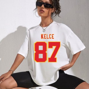 May include: White oversized t-shirt with red and yellow lettering that says "KELCE 87".