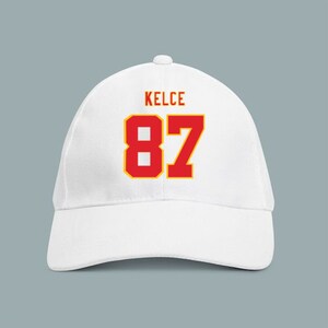 May include: White baseball cap with the name "Kelce" and the number "87" in red with a yellow outline.