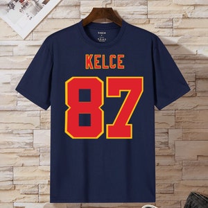 May include: Navy blue t-shirt with the name "KELCE" and the number "87" printed in red with a yellow outline.