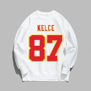 May include: White sweatshirt with a red and yellow number 87 and the name "KELCE" printed on the front.