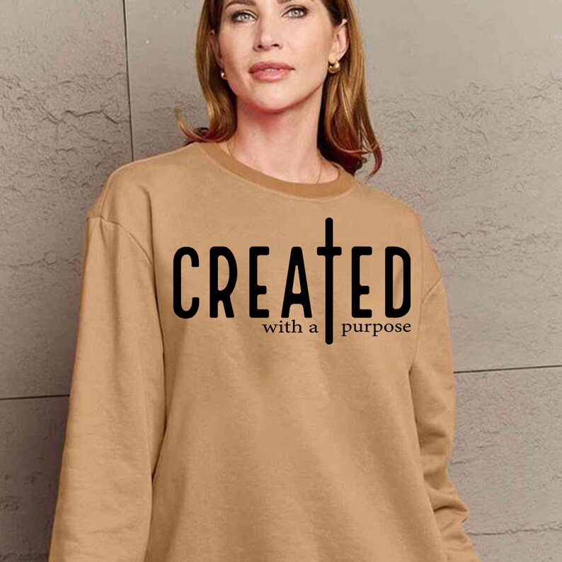 May include: A tan sweatshirt with the text "CREATED with a purpose" and a cross graphic printed on the front.
