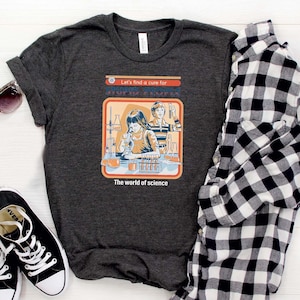 May include: Dark gray t-shirt with a retro science graphic featuring the text "Let's find a cure for..." and "The world of science." The image includes black and white sneakers, sunglasses, and a black and white plaid shirt.