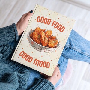 Puede incluir: Una libreta amarilla y naranja con el texto "Good Food, Good Mood" y una imagen de pollo frito en un tazón blanco.