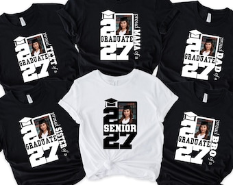 May include: A collection of five t-shirts featuring a graduation theme. Four black shirts display the text 'proud [family member] of a GRADUATE 27' with a photo of a graduate. One white shirt features the text 'SENIOR 27' and a graduate photo.