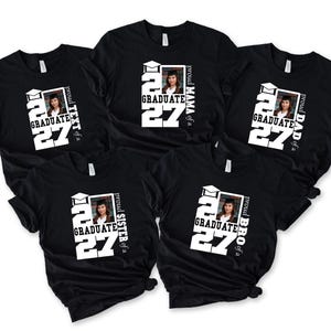 Op de afbeelding: Vijf zwarte t-shirts met korte mouwen en een wit grafisch ontwerp met een afstudeerhoed-icoon, het getal 27 en een foto van een afgestudeerde. Elk shirt bevat tekst die familierollen identificeert: MAMA, DAD, SISTER, BRO en TEXT of a graduate.