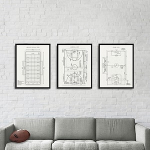 Puede incluir: Tres impresiones enmarcadas en negro de diagramas de campos deportivos. Las impresiones están colgadas en una pared de ladrillo blanco sobre un sofá gris. Las impresiones están tituladas "Campo de fútbol americano", "Cancha de baloncesto" y "Campo de fútbol".