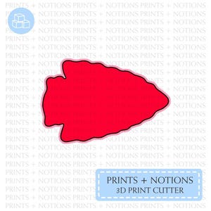 May include: A red arrowhead-shaped 3D print cutter. The cutter is outlined in black and has a slightly textured surface. The text "PRINTS + NOTIONS 3D PRINT CUTTER" is in a blue box with a white border.