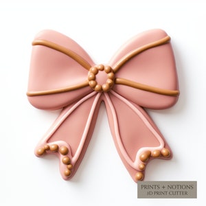 May include: A pink bow cookie cutter with brown lines and brown bead accents.  PRINTS + NOTIONS 3D PRINT CUTTER.