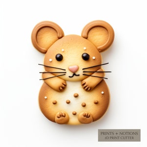 May include: A brown and white cookie shaped like a mouse with black eyes and a pink nose. The cookie has white sprinkles on it and is decorated with brown icing. The cookie is on a white background.  PRINTS + NOTIONS 3D PRINT CUTTER