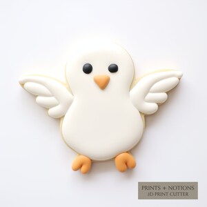 May include: A white cookie decorated with icing to look like a dove. The dove has black eyes, an orange beak, and orange feet.