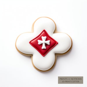 May include: A white cookie with red icing in the shape of a diamond with a white cross in the center. The cookie is shaped like a four-leaf clover. The text "PRINTS + NOTIONS 3D PRINT CUTTER" is visible at the bottom of the image.