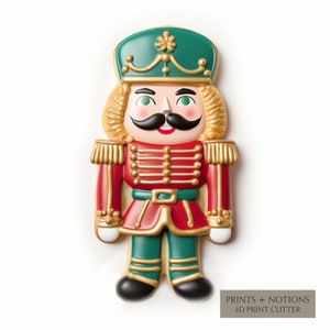 May include: A cookie cutter in the shape of a toy soldier nutcracker. The nutcracker has a green hat, gold hair, a black mustache, and a red uniform with gold accents. The text "PRINTS + NOTIONS 3D PRINT CUTTER" is at the bottom.