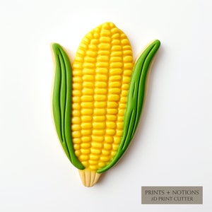 May include: A yellow and green cookie cutter shaped like an ear of corn. The cutter is designed for making cookies and other baked goods.  PRINTS + NOTIONS 3D PRINT CUTTER