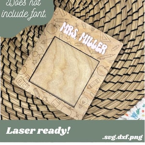 Puede incluir: Un marco de madera cortado con láser con un diseño de temática escolar. El marco tiene un espacio en blanco en el centro para una foto u otra obra de arte. El texto "MRS. MILLER" está grabado en el marco. El marco está listo para ser utilizado para el escritorio de un maestro o la decoración de un aula.