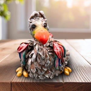 May include: A detailed figurine of a Dodo bird, featuring a large red beak, yellow feet, and colorful feathers. The bird is primarily brown and gray, with accents of red, blue, and green. The sculpture is placed on a wooden surface.