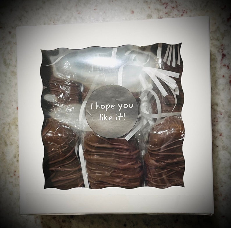 May include: A white gift box with a clear window showing several chocolate-covered treats inside. The box has a white circle sticker with the text "I hope you like it!" on it.
