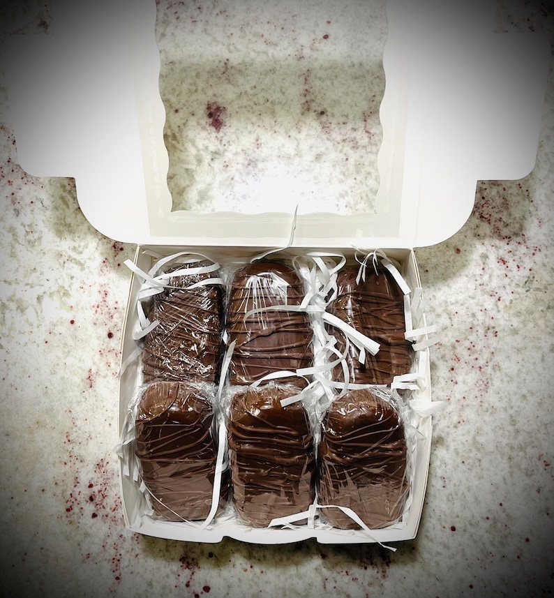 May include: A white box filled with six individually wrapped chocolate bars. The bars are arranged in two rows of three. The bars are all the same size and shape, and they are all wrapped in clear plastic.