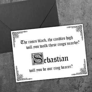 Peut inclure: Une carte blanche avec une inscription gothique noire demandant "Les roses noires, les bougies hautes, marcherez-vous près de ces anneaux ? Sébastien, accepterez-vous d'être notre porteur d'alliances ?"