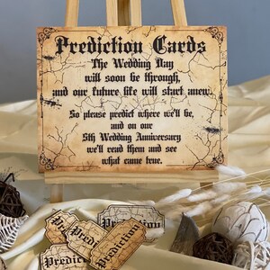 Peut inclure: Un ensemble de cartes de pr&eacute;diction de style vintage avec une texture vieillie de type parchemin. Les cartes portent le texte "Prediction Cards" dans une police d&eacute;corative. Le texte sur le panneau indique : "The Wedding Day will soon be through, and our future life will start anew. So please predict where we'll be, and on our 5th Wedding Anniversary we'll read them and see what came true."