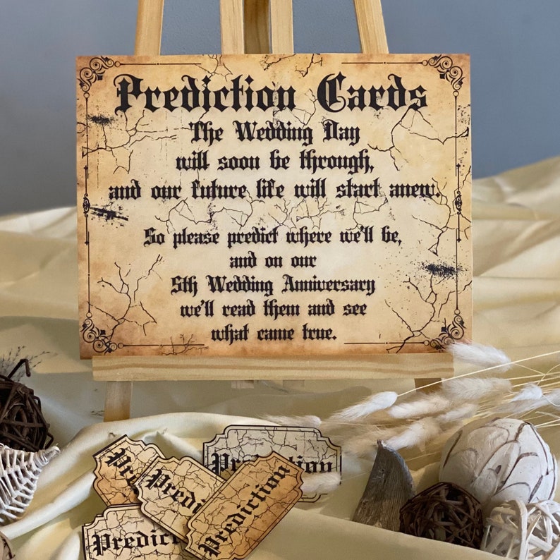 Peut inclure: Un ensemble de cartes de pr&eacute;diction de style vintage avec une texture vieillie de type parchemin. Les cartes portent le texte "Prediction Cards" dans une police d&eacute;corative. Le texte sur le panneau indique : "The Wedding Day will soon be through, and our future life will start anew. So please predict where we'll be, and on our 5th Wedding Anniversary we'll read them and see what came true."