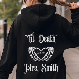 以下が含まれることがあります： 「Til Death」という白い文字と、ハートと日付「09-12-2024」と「Mrs. Smith」という文字が書かれた黒いフード付きスウェットシャツ。